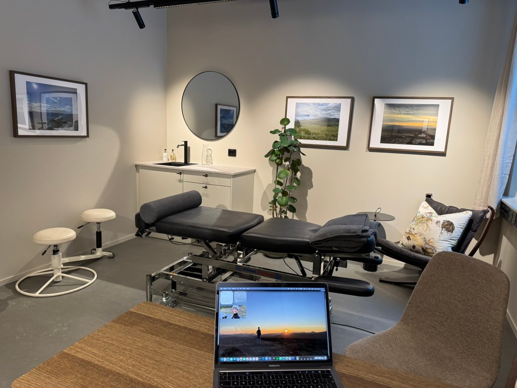 An office room with a laptop and a table in the foreground, featuring various pieces of furniture, artwork, and plants in ...